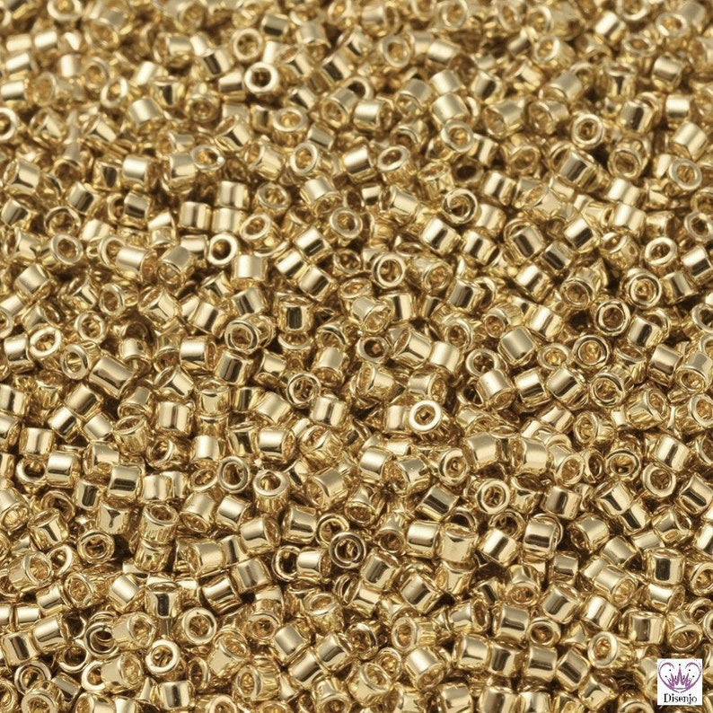 May include: A close-up view of a large quantity of small, gold-colored seed beads. The beads are round and have a smooth, shiny finish.