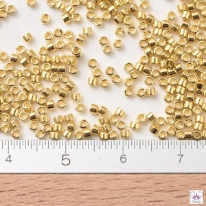 May include: A close-up of a large quantity of small, gold-colored metal beads scattered on a white surface. A ruler is visible in the bottom of the image, with markings for inches 4, 5, 6, and 7.