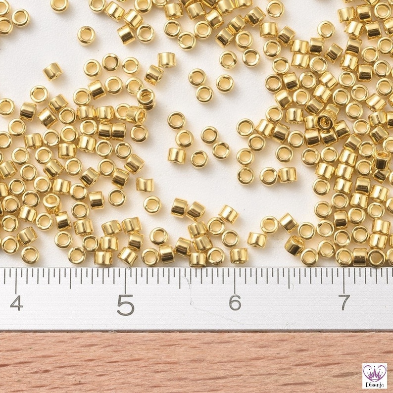 May include: A close-up of a large quantity of small, gold-colored metal beads scattered on a white surface. A ruler is visible in the bottom of the image, with markings for inches 4, 5, 6, and 7.