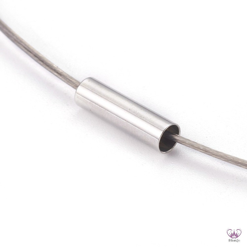 May include: Close-up of a silver metal tube with a thin silver wire threaded through it. The tube is a connector for a necklace or bracelet.