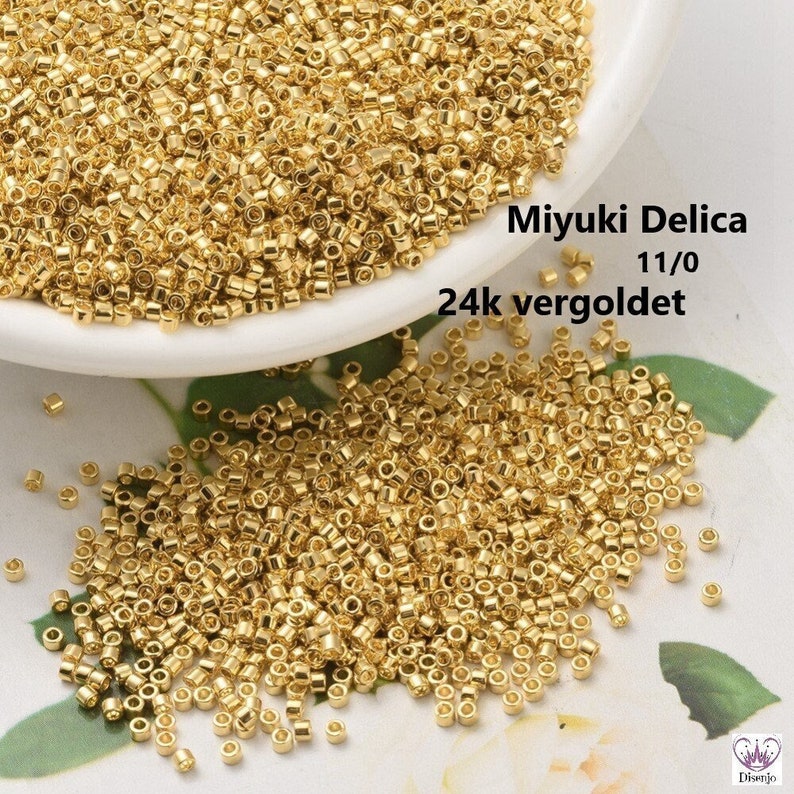 May include: A close-up of a pile of small, gold-colored beads. The beads are round and have a smooth, shiny finish. The text "Miyuki Delica 11/0 24k vergoldet" is visible in the image.