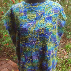 Könnte beinhalten: Ein blaues, grünes und violettes Strickponcho mit Fransenbesatz. Das Poncho ist aus einem weichen, strukturierten Garn gefertigt und hat eine lockere, fließende Passform.