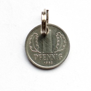 May include: A silver German 1 Pfennig coin from 1982 with a key ring attached. The coin features a stylised depiction of the Brandenburg Gate.