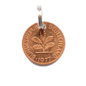 Könnte beinhalten: Eine kupferfarbene Münze von 1977 mit dem Text "BUNDESREPUBLIK DEUTSCHLAND" und einem Pflanzendesign. Die Münze ist an einem silberfarbenen Schlüsselring befestigt. Das Design der Münze zeigt eine Pflanze mit Blättern.
