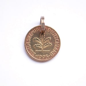 Könnte beinhalten: Ein goldfarbener Münzanhänger mit einer Schlaufe für eine Kette. Die Münze trägt den Text "BUNDESREPUBLIK DEUTSCHLAND" und das Jahr "1995" um ein zentrales Pflanzendesign. Der Anhänger befindet sich auf weißem Hintergrund.