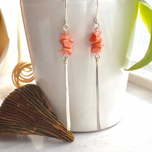 Puede incluir: Un par de pendientes de plata con detalles de piedra de coral rosa. Los pendientes tienen varillas largas y delgadas de plata con un grupo de piedras de coral en la parte superior.