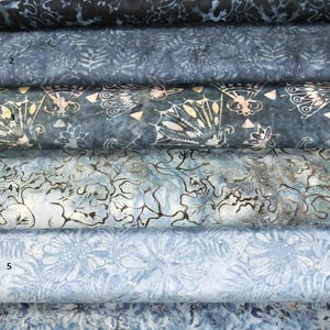 Peut inclure: Six rouleaux de tissus bleus à motifs variés. Les tissus présentent divers motifs, notamment floraux, de feuilles et abstraits. La palette de couleurs va du bleu marine foncé au bleu clair, certains tissus ayant des accents blancs ou crème.