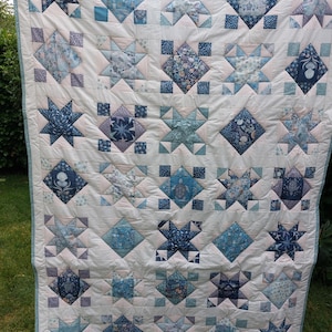 Puede incluir: Una colcha de patchwork con un patrón repetitivo de bloques de estrellas y diamantes en varios tonos de azul, blanco y gris claro. La tela muestra diversos estampados náuticos y florales, incluyendo tortugas marinas, conchas y motivos botánicos.