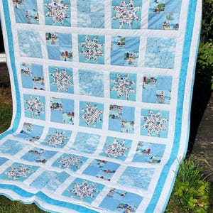 May include: A blue and white patchwork quilt with a nautical theme. The quilt is made up of squares with different designs, including stars, seashells, and lighthouses. The quilt is edged with a blue border.