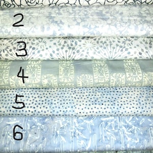 以下が含まれることがあります： さまざまな模様の7つの生地サンプルが積み重ねられています。一番上の生地は、白黒のバラのデザインです。他の生地には、青、グレー、白の色合いのフローラル、ドット、幾何学模様が含まれています。生地はきちんと丸められています。