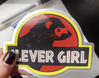 Pode incluir: Adesivo prateado com um design de furão preto sobre fundo vermelho, com borda amarela. O texto "CLEVER GIRL" está escrito em branco.