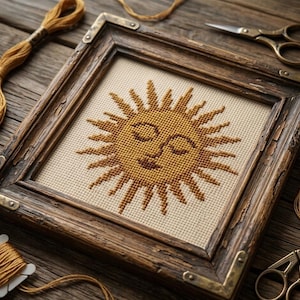 May include: A framed cross-stitch of a smiling sun with yellow and brown thread. The artwork is set in a distressed wooden frame with metal corner brackets. Embroidery thread and scissors are visible.