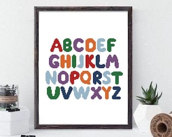May include: A framed cross-stitch design featuring the alphabet in colorful, rounded letters. The letters are arranged in three rows, with each letter a different color.