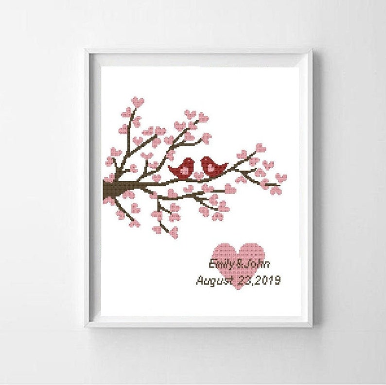 Puede incluir: Obra de arte en punto de cruz enmarcada que representa dos p&aacute;jaros rojos posados en una rama marr&oacute;n con flores rosas en forma de coraz&oacute;n. Debajo, dos corazones rosas y el texto "Emily & John August 23, 2019".