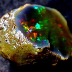 May include: A rough, natural opal gemstone with a vibrant green, blue, and red iridescent sheen. The opal is embedded in a brown, rocky matrix.
