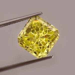 May include: A bright yellow gemstone with a faceted cut. The gemstone is held by a pair of tweezers.