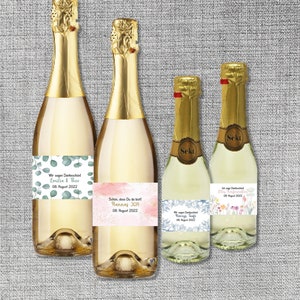 Könnte beinhalten: Vier Flaschen Sekt mit personalisierten Etiketten. Die Etiketten zeigen Blumen- und botanische Designs mit dem Text "Wir sagen Dankeschön! Emilia & Theo 08. August 2022", "Schön, dass Du da bist! Hannas JGA 08. August 2022", "Henrys Taufe 08. August 2022" und "Ich sage Dankeschön! Ellens Konfirmation 08. August 2022".