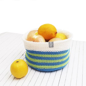 Può includere: Un cesto di uncinetto bianco con strisce blu e verdi, pieno di limoni e cipolle. Il cesto ha un'etichetta bianca con la parola "enio" su di essa.