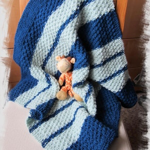 Peut inclure: Une couverture pour b&eacute;b&eacute; en tricot ray&eacute;e bleu et bleu clair avec un jouet en peluche en forme de girafe sur le dessus.