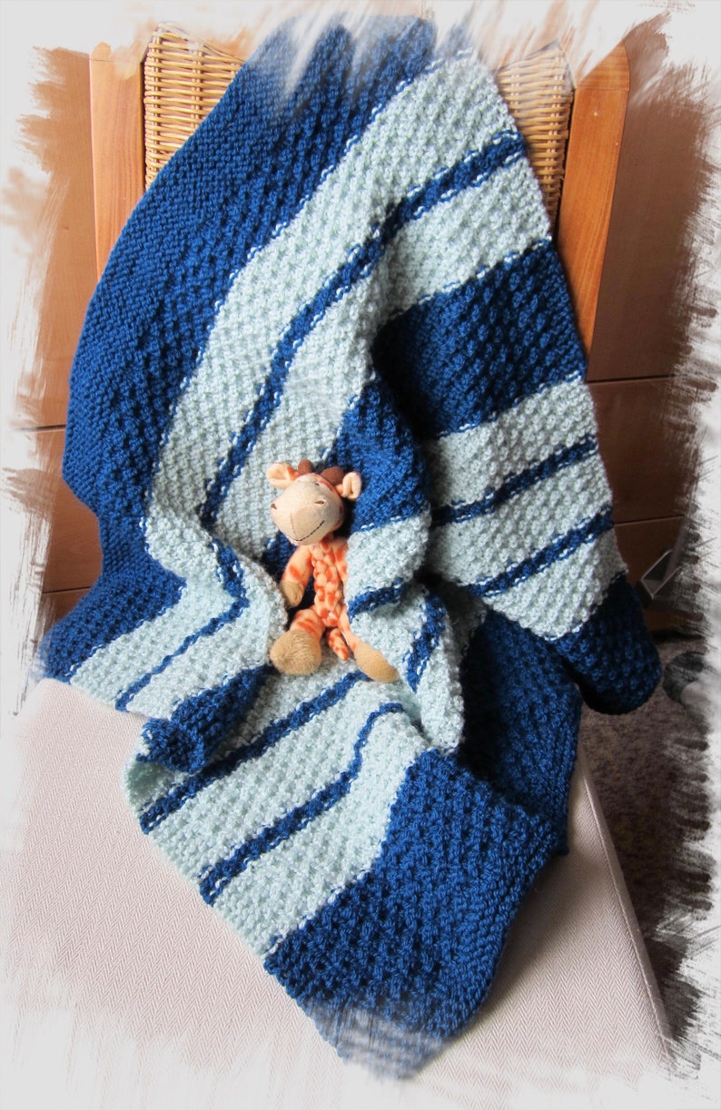 Peut inclure: Une couverture pour b&eacute;b&eacute; en tricot ray&eacute;e bleu et bleu clair avec un jouet en peluche en forme de girafe sur le dessus.
