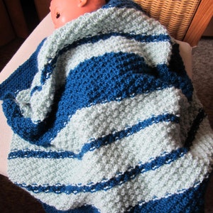 Peut inclure: Une couverture pour b&eacute;b&eacute; en tricot ray&eacute;e bleu et bleu clair. La couverture est faite avec un point textur&eacute; et a une sensation douce et confortable.