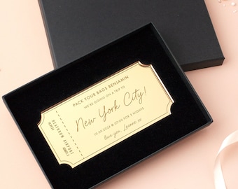 May include: A gold-coloured ticket with the text "PACK YOUR BAGS BENJAMIN WE'RE GOING ON A TRIP TO New York City! 10.09.2024 07:00 FOR 3 NIGHTS love you, Leanne xx" The ticket is in a black box with a black velvet lining.