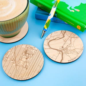 May include: Three wooden coasters with engraved maps and the words "Engaged", "Married", and "TUS" on a light blue surface.