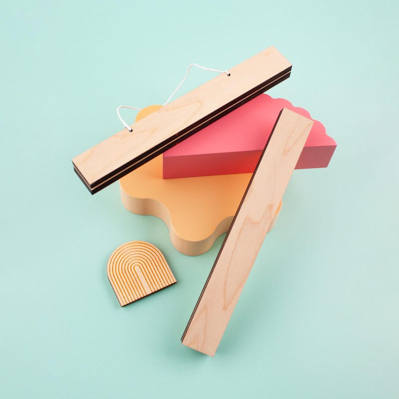 May include: A set of wooden wall decor pieces in various shapes and sizes. The set includes a long rectangular piece, a smaller rectangular piece, a curved piece, and a rainbow-shaped piece. The pieces are all made of natural wood and have a light brown color.