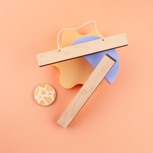 May include: Two wooden picture frames with a black border, one is lying on top of the other. The frames are on a peach colored background with a light blue and a yellow shape behind them. A small wooden circle with a white and brown pattern is in the lower left corner.