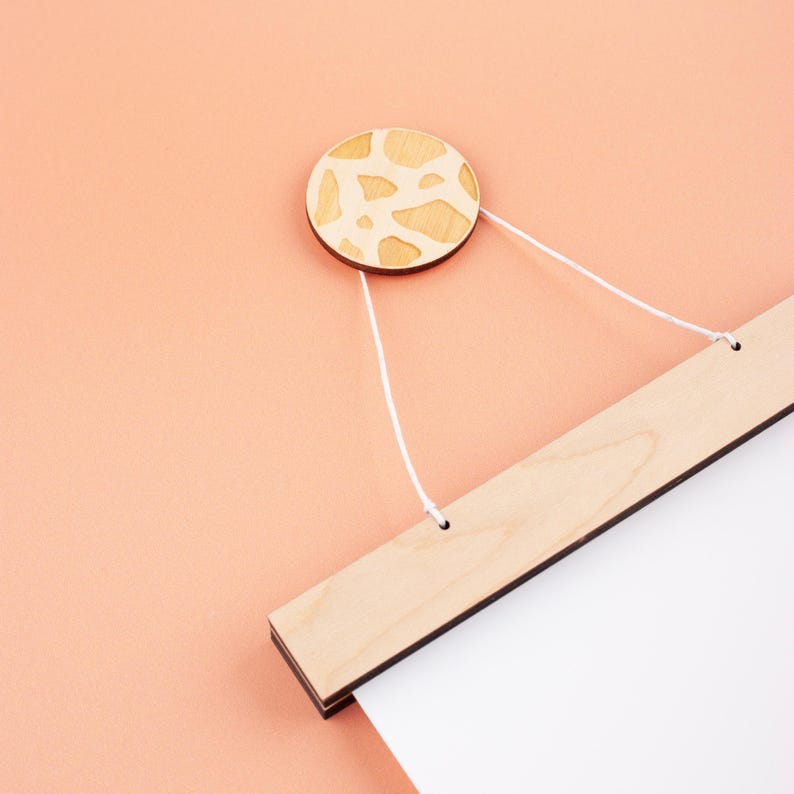 May include: A wooden hanging system with a white string and a round wooden knob with a light brown and white patterned design. The hanging system is attached to a white poster.