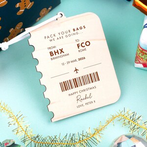 May include: A wooden luggage tag with a travel theme. The tag is light-colored with brown text that reads "PACK YOUR BAGS WE ARE GOING..." and includes flight details from BHX Birmingham to FCO Rome, dated March 12-29, 2026. It says "HAPPY CHRISTMAS" and has a personal message.