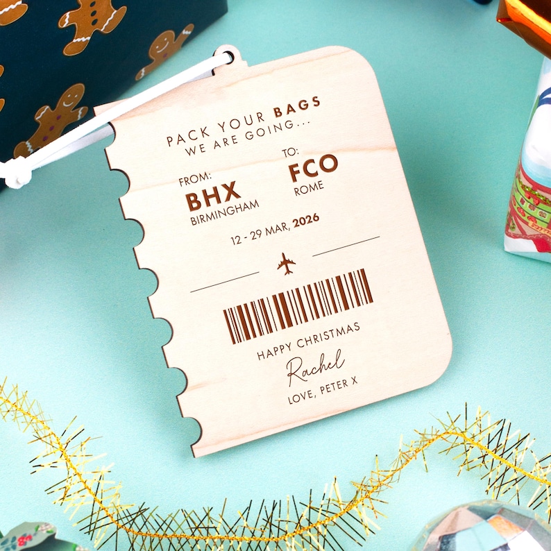 May include: A wooden luggage tag with a travel theme. The tag is light-colored with brown text that reads "PACK YOUR BAGS WE ARE GOING..." and includes flight details from BHX Birmingham to FCO Rome, dated March 12-29, 2026. It says "HAPPY CHRISTMAS" and has a personal message.