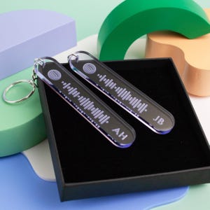 May include: Two clear acrylic keychains with a black background and a white Spotify barcode design. The keychains are engraved with the initials "AH" and "JB".