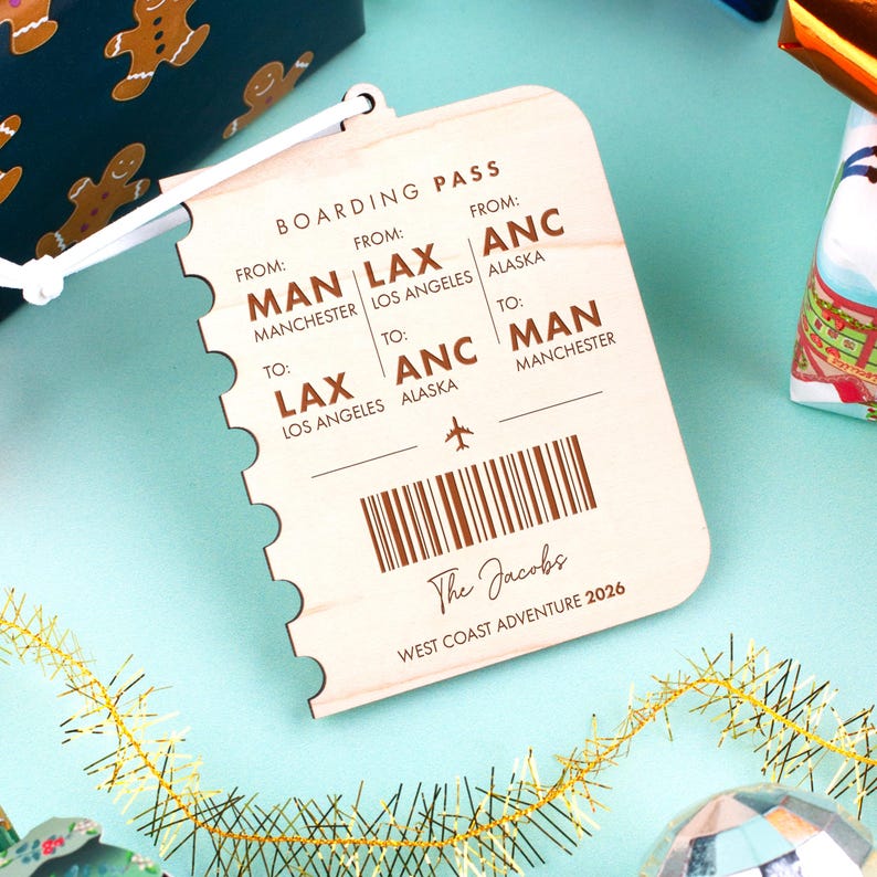May include: Wooden boarding pass-shaped ornament with the text "BOARDING PASS" and flight details from Manchester to Los Angeles and Alaska. The ornament includes the text "The Jacobs West Coast Adventure 2026".
