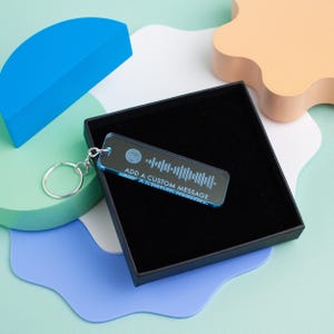 May include: A blue acrylic keychain with a silver key ring. The keychain has a white engraved Spotify logo and a barcode with the text "ADD A CUSTOM MESSAGE".