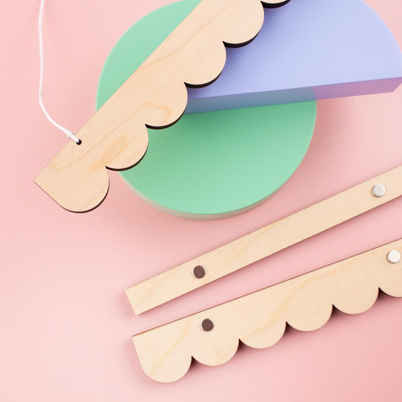 May include: Two wooden strips with scalloped edges and metal accents. The strips are light brown and have a natural wood finish. The strips are arranged in a way that suggests they are part of a mobile or hanging decoration.