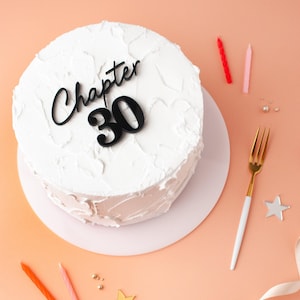 Peut inclure: Gâteau blanc avec glaçage noir et un dessus en acrylique noir qui dit "Chapitre 30".