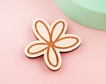 May include: A wooden flower-shaped craft element with five petals. The petals have a light wood color with a darker brown outline and center. The background is a soft pink, with a mint green semi-circle in the upper right corner.