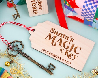 May include: A wooden tag with the text "Santa's MAGIC Key FOR GEORGIA & LEO" and a decorative key. The tag is tied with a red and white string. A smaller tag reads "Reindeer Treats". Festive holiday decor.