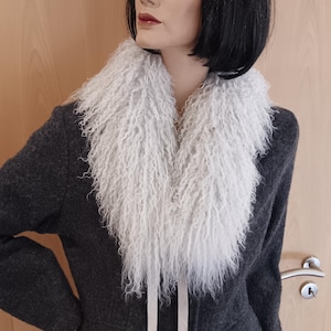 May include: A dark grey blazer with a white, fluffy collar. The blazer has two front pockets and is worn on a mannequin with a black wig. The collar is tied with two white ribbons.