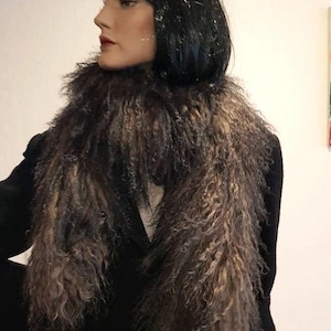 Może przedstawiać: Brązowo-czarny szalik z futra narzucony na czarną kurtkę. Szalik ma długi, teksturowany wygląd z różnymi odcieniami brązu i czerni. Manekin ma na sobie czarną perukę i czerwoną szminkę.