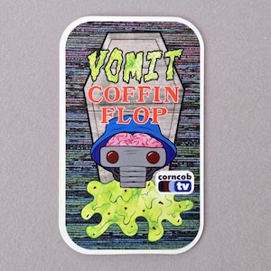May include: A rectangular sticker featuring the text "VOMIT COFFIN FLOP" above a cartoon brain wearing a blue hat and robot-like face. A green, vomit-like substance is below the character, with the "corncob tv" logo in the bottom right.