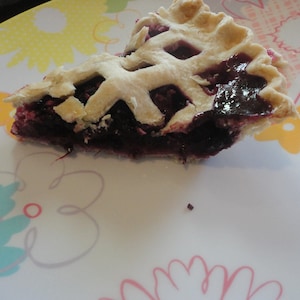 May include: A slice of blueberry pie with a lattice crust on a white plate with a floral design.