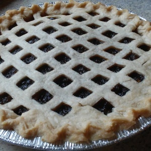 May include: A homemade pie with a lattice crust and a dark brown filling. The pie is in a silver foil pie pan.