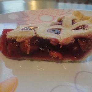 May include: A slice of cherry pie with a flaky crust and a bright red cherry filling.