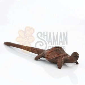 May include: A brown wooden smoking pipe carved into the shape of a turtle. The long, slender stem features etched geometric patterns and a textured scale design. The turtle shell forms the bowl of the pipe, with the head and flippers extending outward.