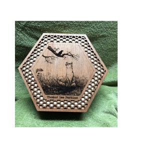 May include: A wooden, hexagonal box with a laser-etched design. The design features a fox looking up at a crow perched on a branch. The box has a honeycomb pattern around the central image and the text "Thomas Lee Perkins" at the bottom.