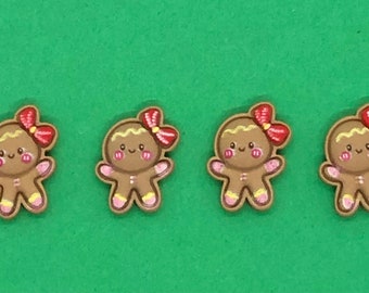 May include: Four gingerbread man-shaped embellishments with red bows and pink accents. The gingerbread men have smiling faces and are set against a green background. These are likely for crafting or holiday decor.