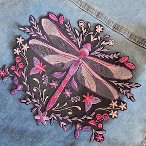 May include: Embroidered dragonfly patch with a black background, surrounded by pink and purple flowers and leaves. The dragonfly has purple and pink wings and a red body. The text "Style I Glow" is at the bottom.