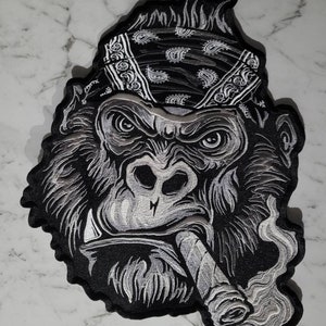Puede incluir: Un parche bordado en blanco y negro de un gorila con un pañuelo en la cabeza y fumando un cigarro.